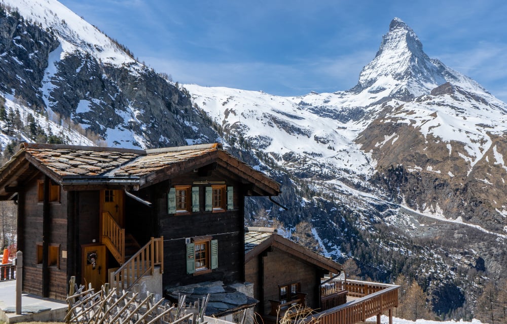 Rustikale Alpen-Deko: Ein gemütliches Holzchalet vor dem imposanten, schneebedeckten Matterhorn, perfekt für Ihre Hüttenabend-Tischdeko.