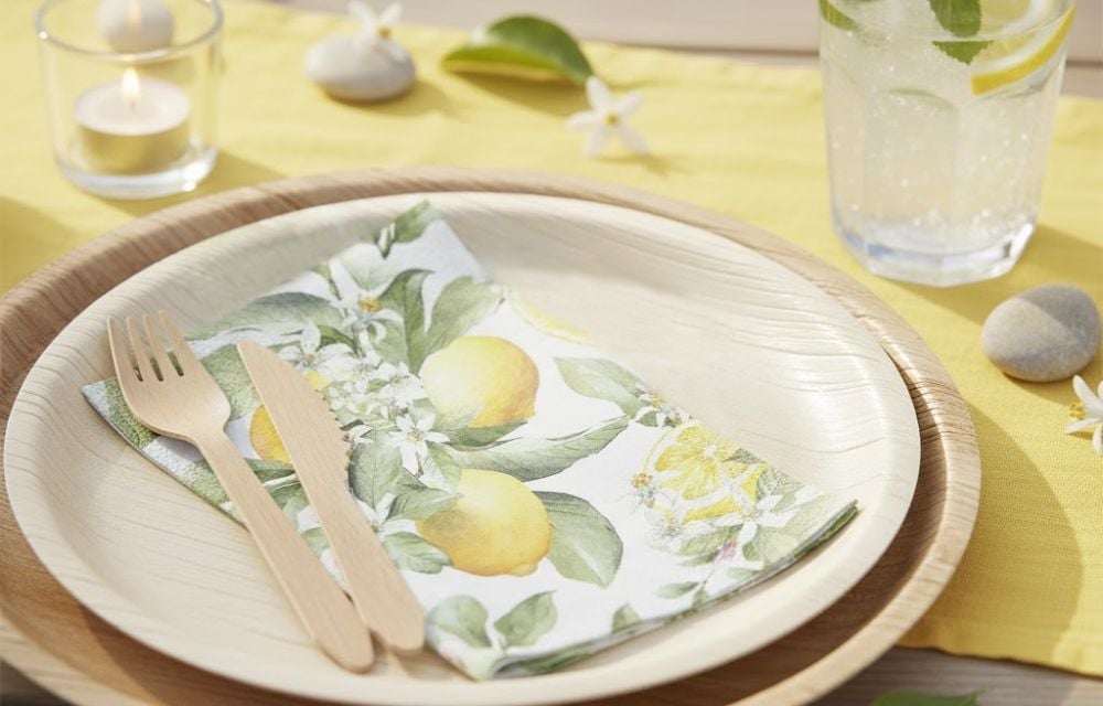 Frische Tischdeko für den Sommer mit umweltfreundlichem Palmblatt-Geschirr, Holzbesteck und einer Serviette mit leuchtendem Zitronenmuster.