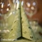 Gefaltete Premium-Serviette in Pistaziengrün aus der Weihnachtsserie Duni Noël Pistachio auf festlich gedecktem Tisch mit Gläsern im Hintergrund.