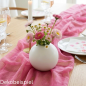 Elegante weiße Kugelvase mit frischen Frühlingsblumen auf einem leuchtend pinkfarbenen Chiffon-Tischläufer arrangiert.