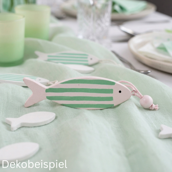 Nahaufnahme von dekorativen Holzfischen in Mint und Weiß auf einem hellgrünen Tischläufer.