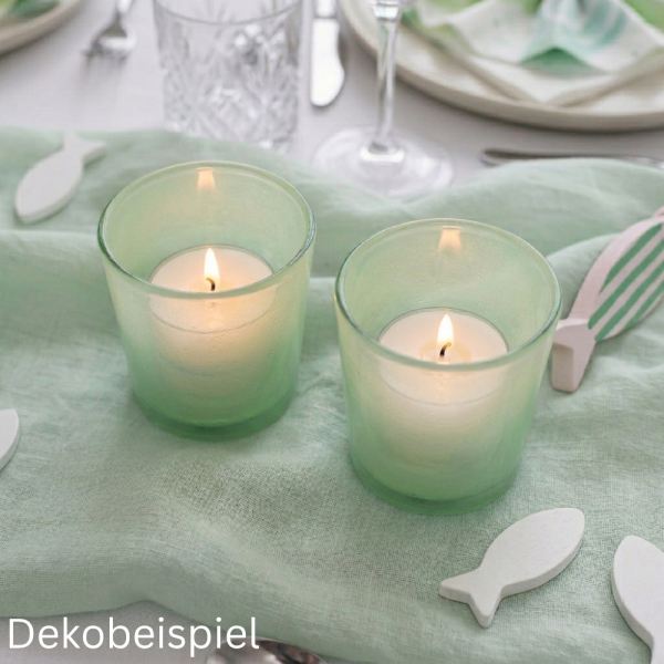 Zwei brennende Teelichter in mintgrünen Glas-Windlichtern auf einem Stoff Tischläufer in Mint.