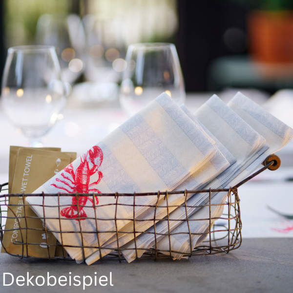 Ein rustikaler Metallkorb gefüllt mit ordentlich geschichteten Hummer-Servietten der Duni Serie Sea Delights auf einem modernen Betontisch.